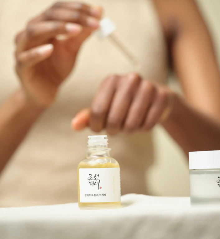 Person applying a skincare product to their hand with a bottle of serum in the foreground.