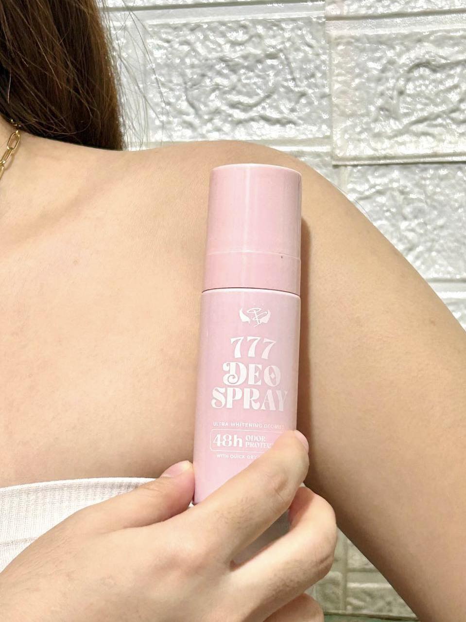 Person holding a pink deodorant spray can against a textured wall.