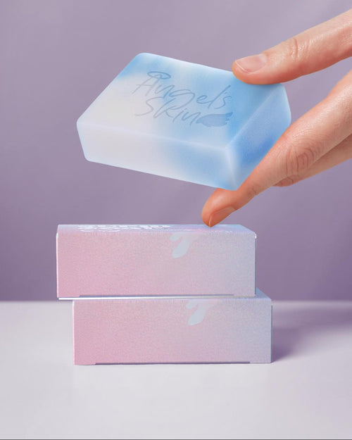 Hand lifting a blue soap bar from a pink soap box against a purple background