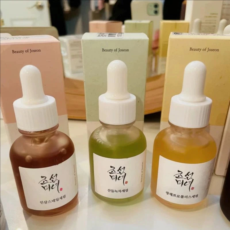 Three dropper bottles with different colored liquids on a table, with 'Beauty of Joseon' packaging in the background.