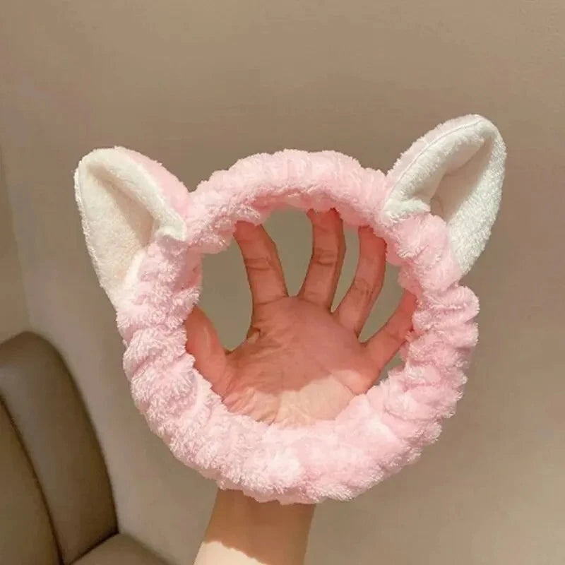 Pink fuzzy headband with cat ears held by a hand against a neutral background