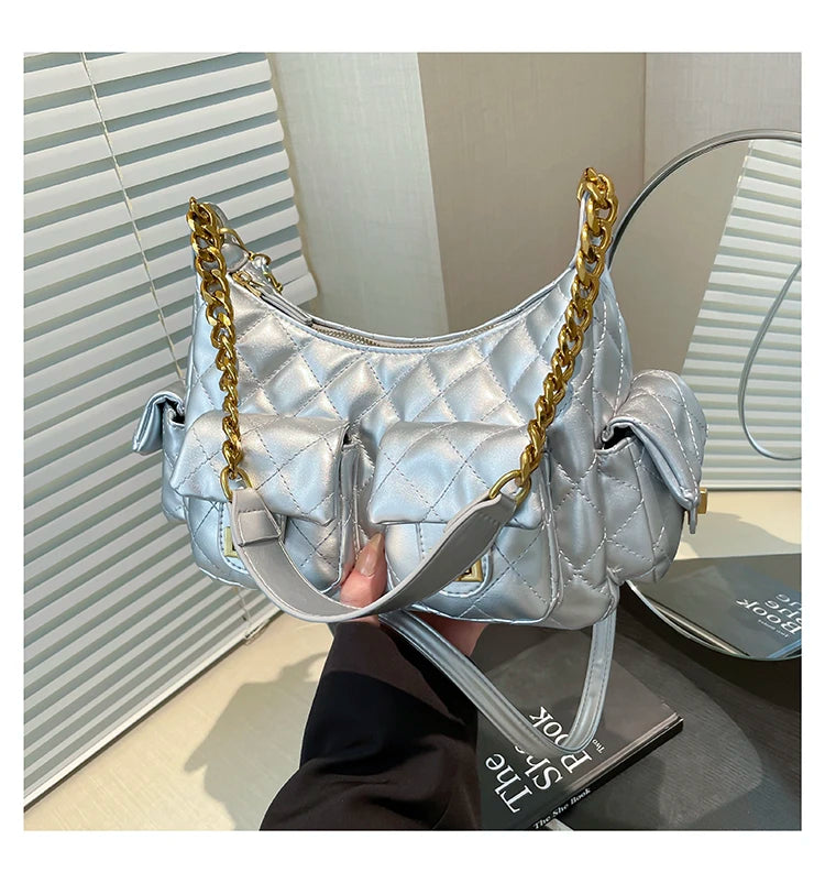 Silver quilted handbag with gold chain strap held by a person in front of a mirror.