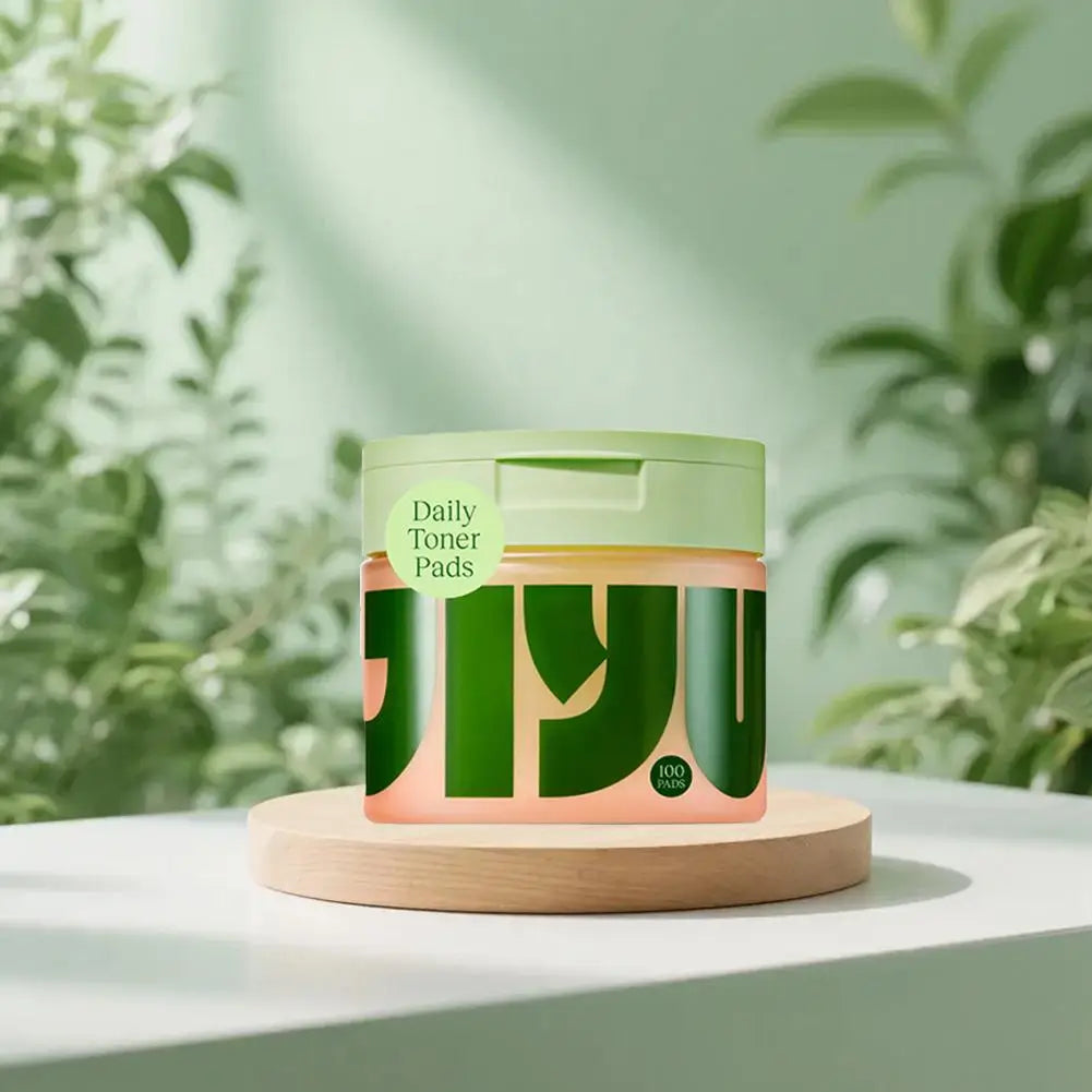 Green container labeled 'Daily Toner Pads' on a light surface with a blurred green plant background