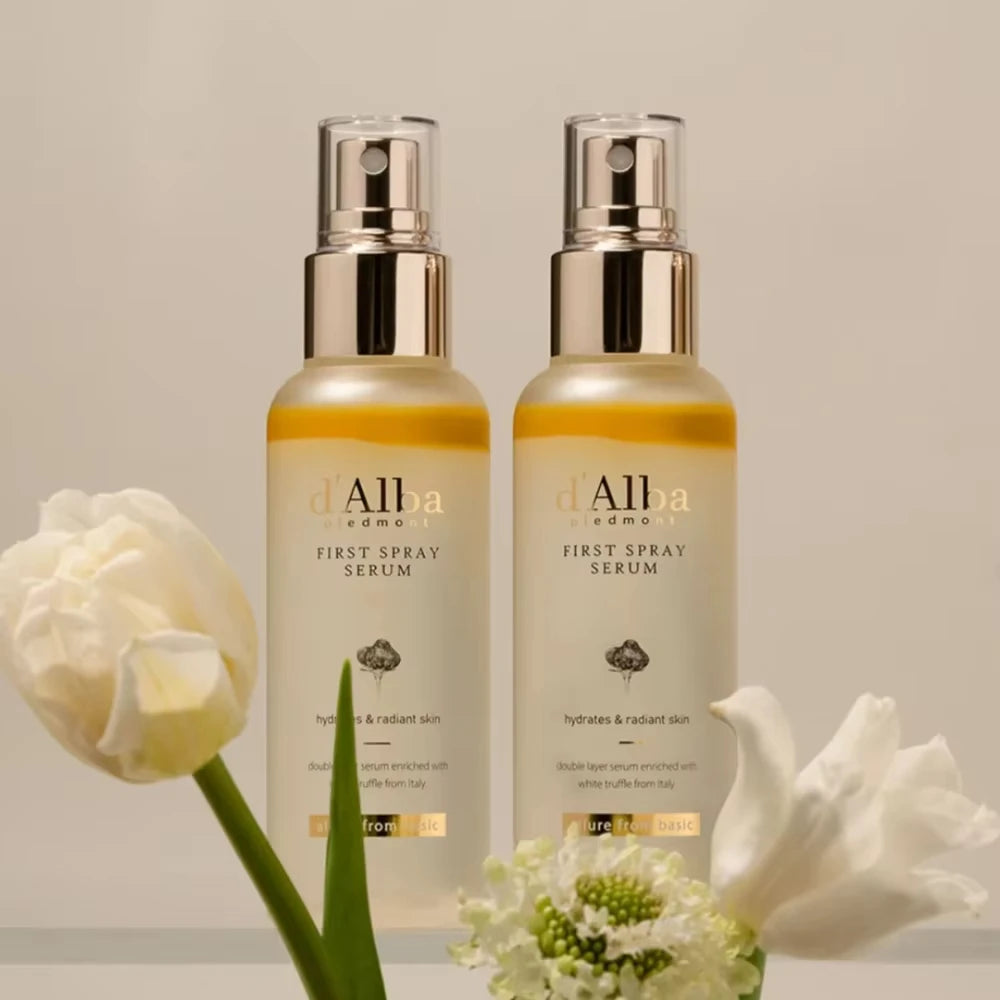 Two bottles of 'Alba Edma' First Spray Serum with flowers on a neutral background