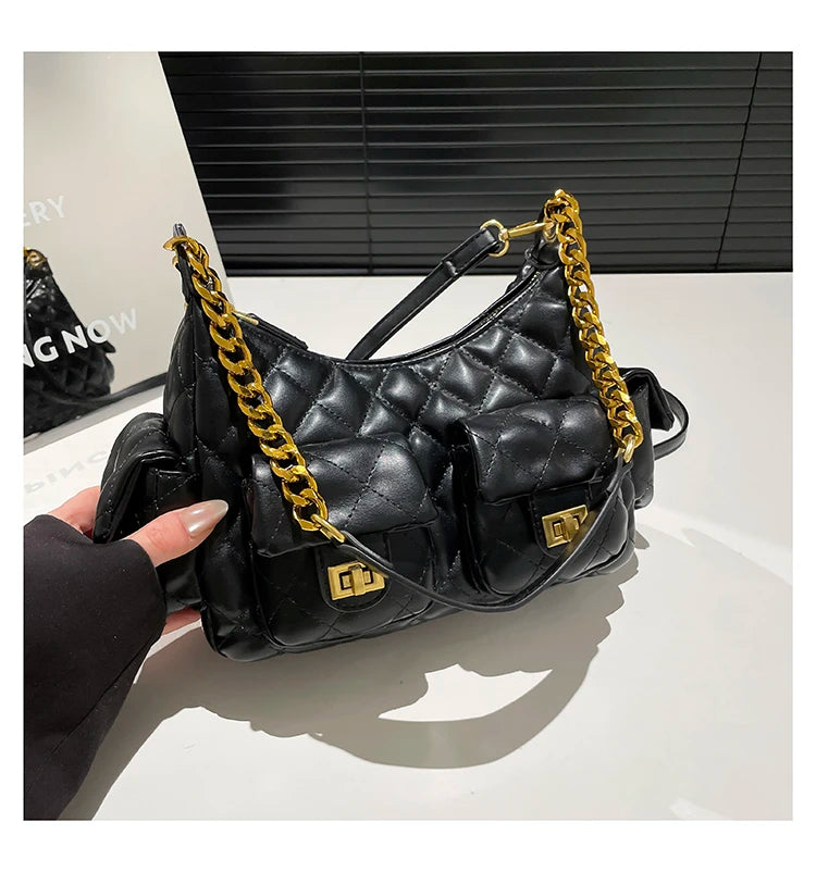 Black handbag with gold chain strap held by a hand on a white surface.