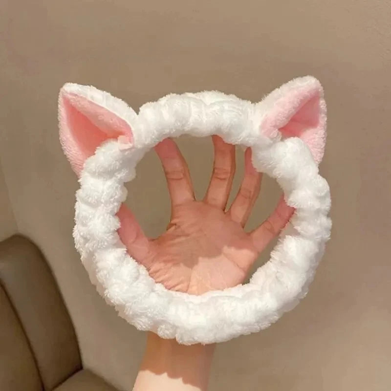 White fluffy headband with pink cat ears held by a hand against a beige background