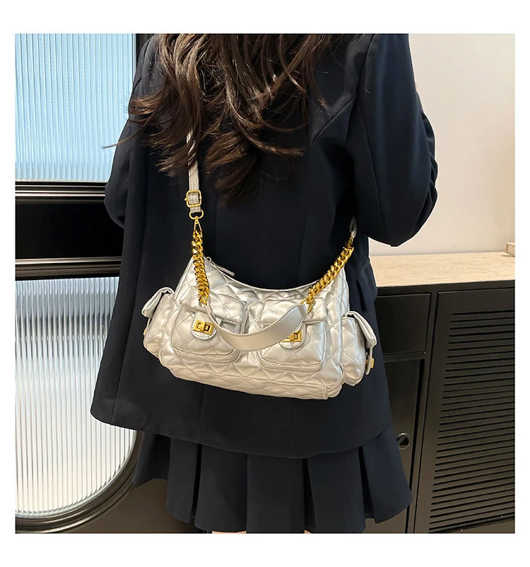 Person wearing a black outfit with a silver handbag featuring gold chain details.
