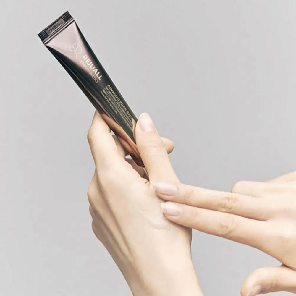 Hand holding a black hair dye tube against a gray background