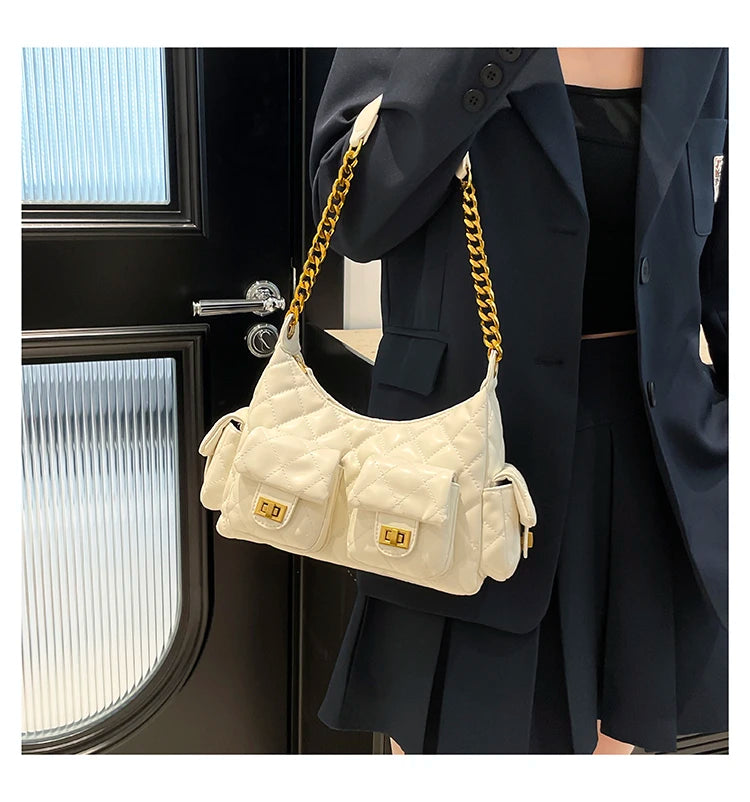 Person holding a cream quilted handbag with gold chain strap in front of a black door.