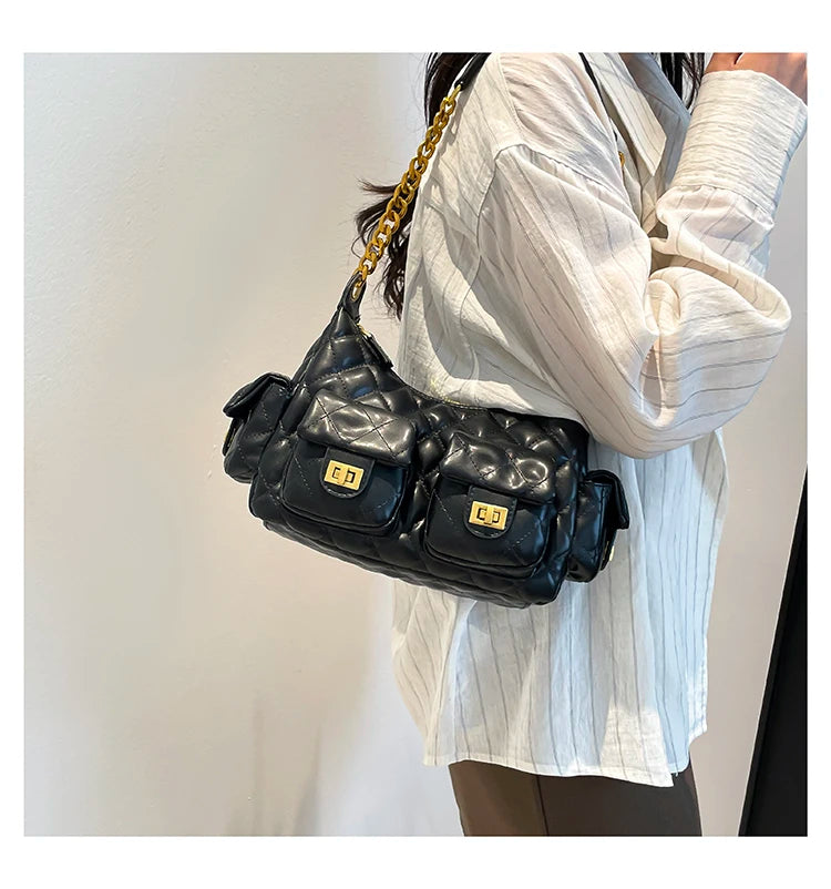 Person wearing a black handbag with gold chain strap on a plain background