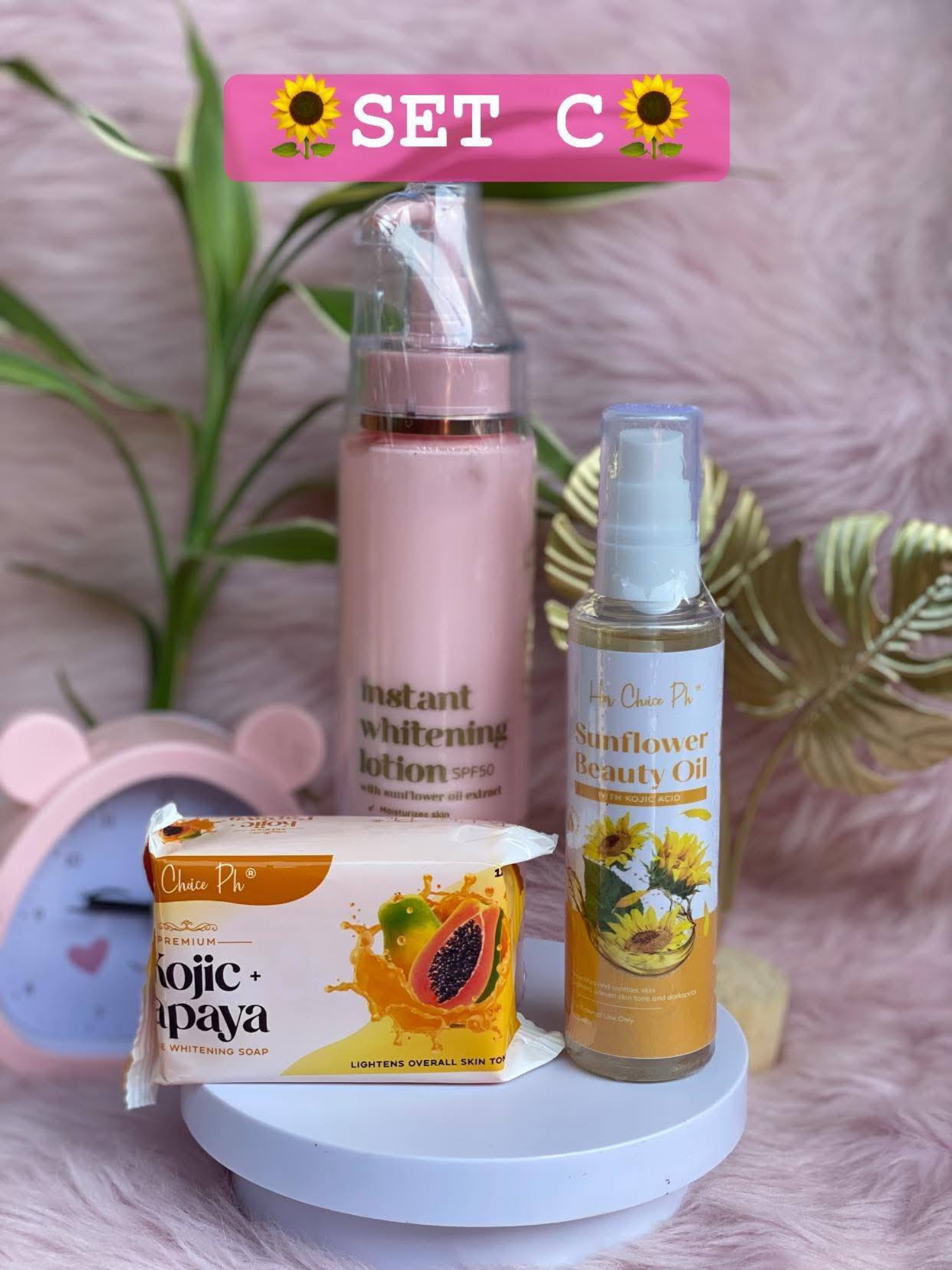 Set of beauty products including a lotion spray, sunflower beauty oil, and soap on a pink surface with decorative elements.