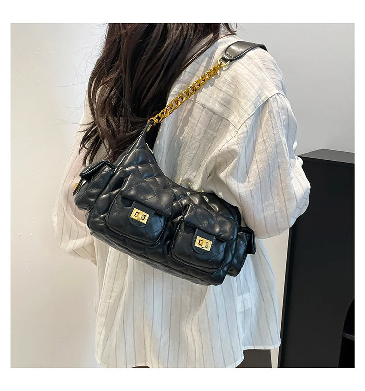 Person wearing a black quilted handbag with gold accents on a plain background