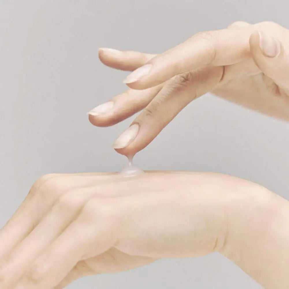 Hand applying lotion to another hand on a gray background