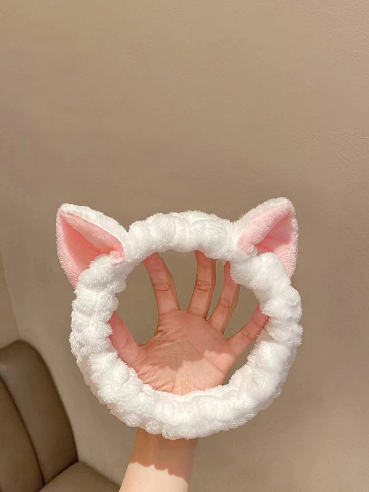 White fluffy headband with pink cat ears held by a hand against a beige background