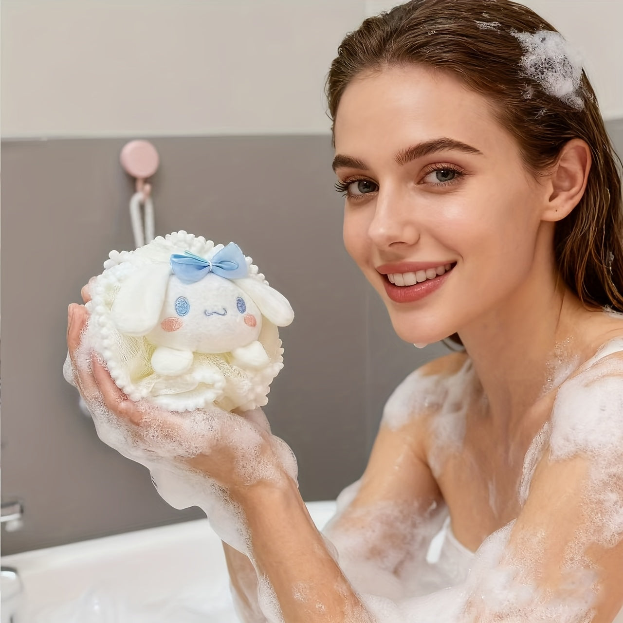 Woman in a bathtub holding a fluffy white toy with a blue bow, surrounded by bubbles.